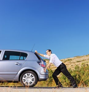Young businessman pushing his car with empty fuel tank, shot with a tilt and shift lens