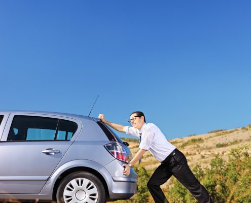 Young businessman pushing his car with empty fuel tank, shot with a tilt and shift lens